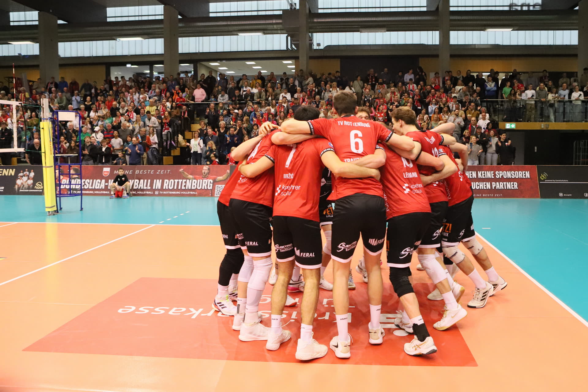 Die Spieler des TV Rottenburg stehen nach dem Spiel im Kreis auf dem Feld, dahinter die volle Halle.