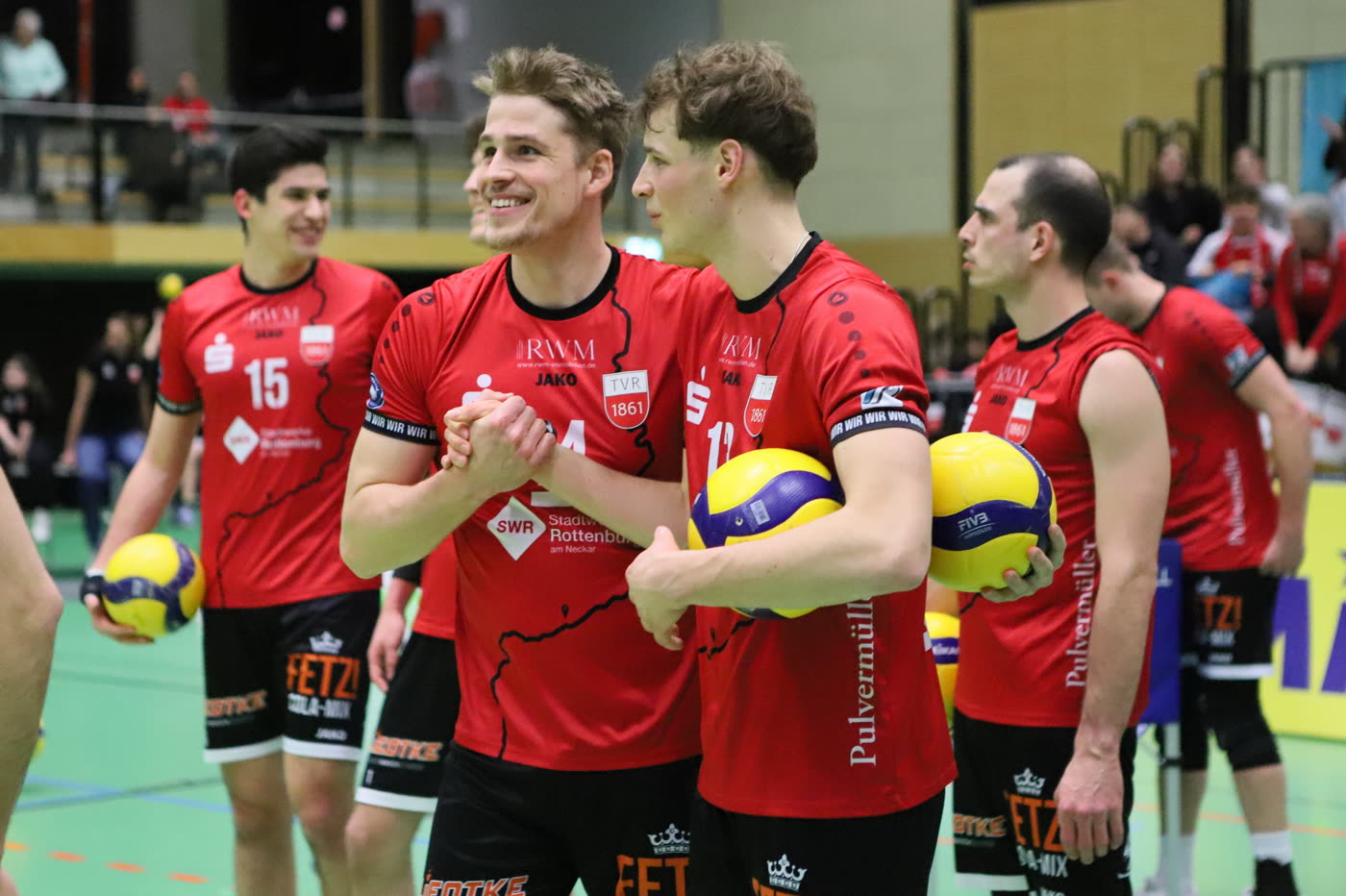 Spieler des TV Rottenburg stehen vor dem Spiel mit Bällen am Rand des Feldes und lachen.